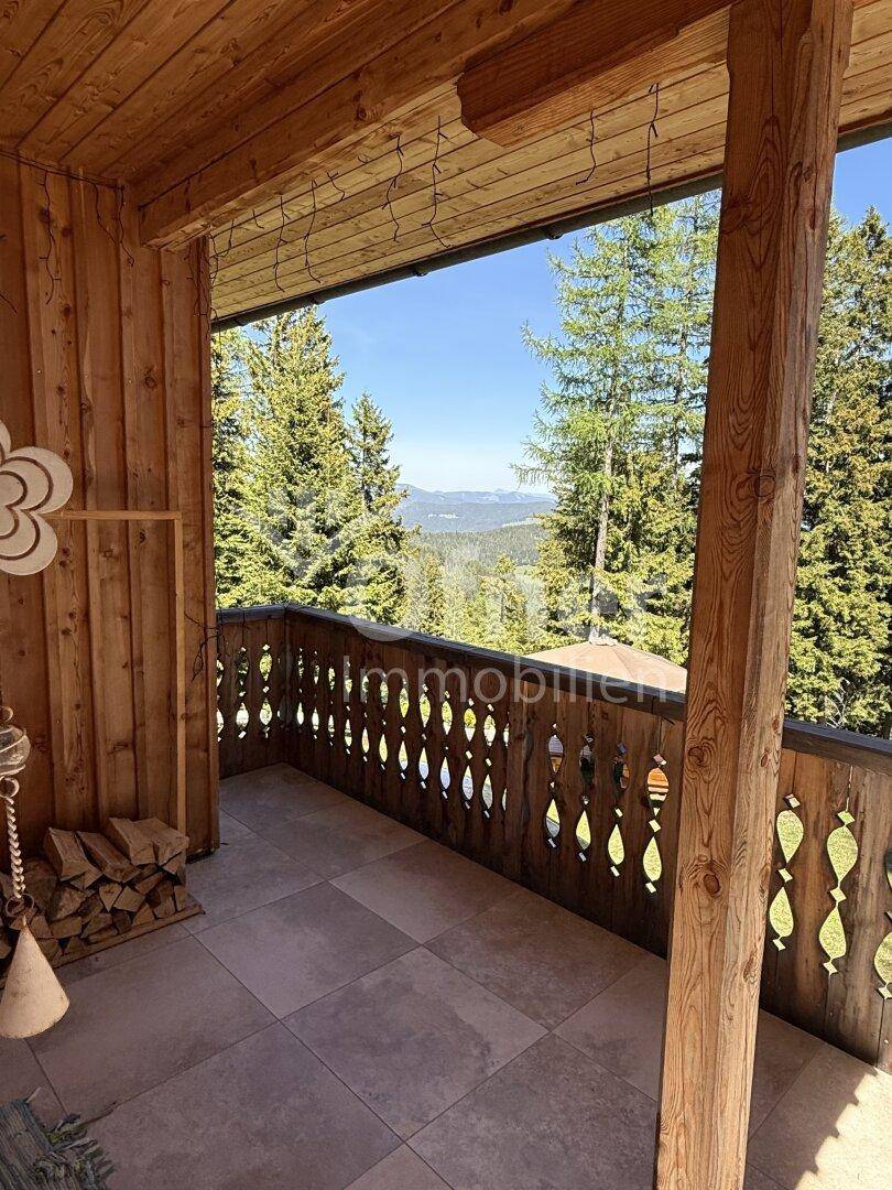 Gemütliche Holzloggia mit Fliesenboden und weitem Blick über die bewaldete Berglandschaft.