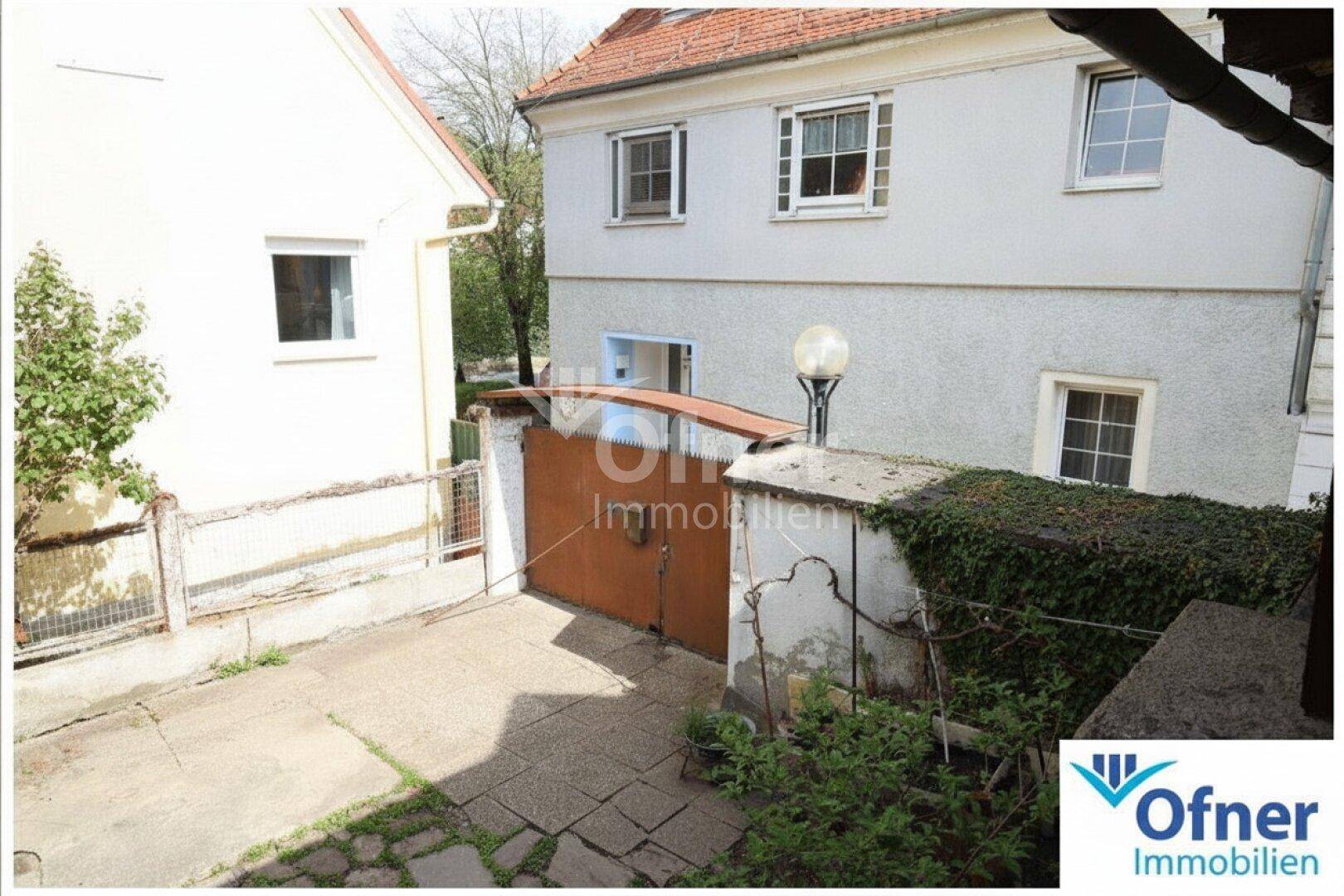 Einfahrt zwischen zwei Gebäuden mit einem alten Tor und Bewuchs an der Wand.