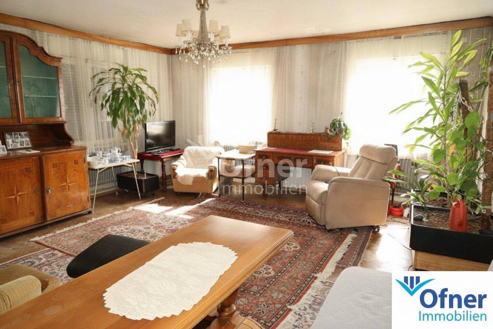 Geräumiges Wohnzimmer mit Teppichboden, Kronleuchter und traditionellen Möbeln, hell durch große Fenster.