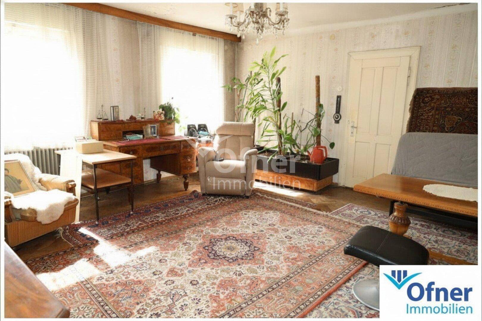 Gemütliches Wohnzimmer mit Schreibtisch, Pflanzen und orientalischem Teppich, gut beleuchtet.