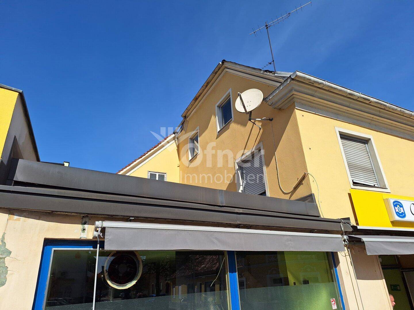 Gelbe Fassade eines Gebäudes mit Satellitenschüssel und Antenne unter blauem Himmel.
