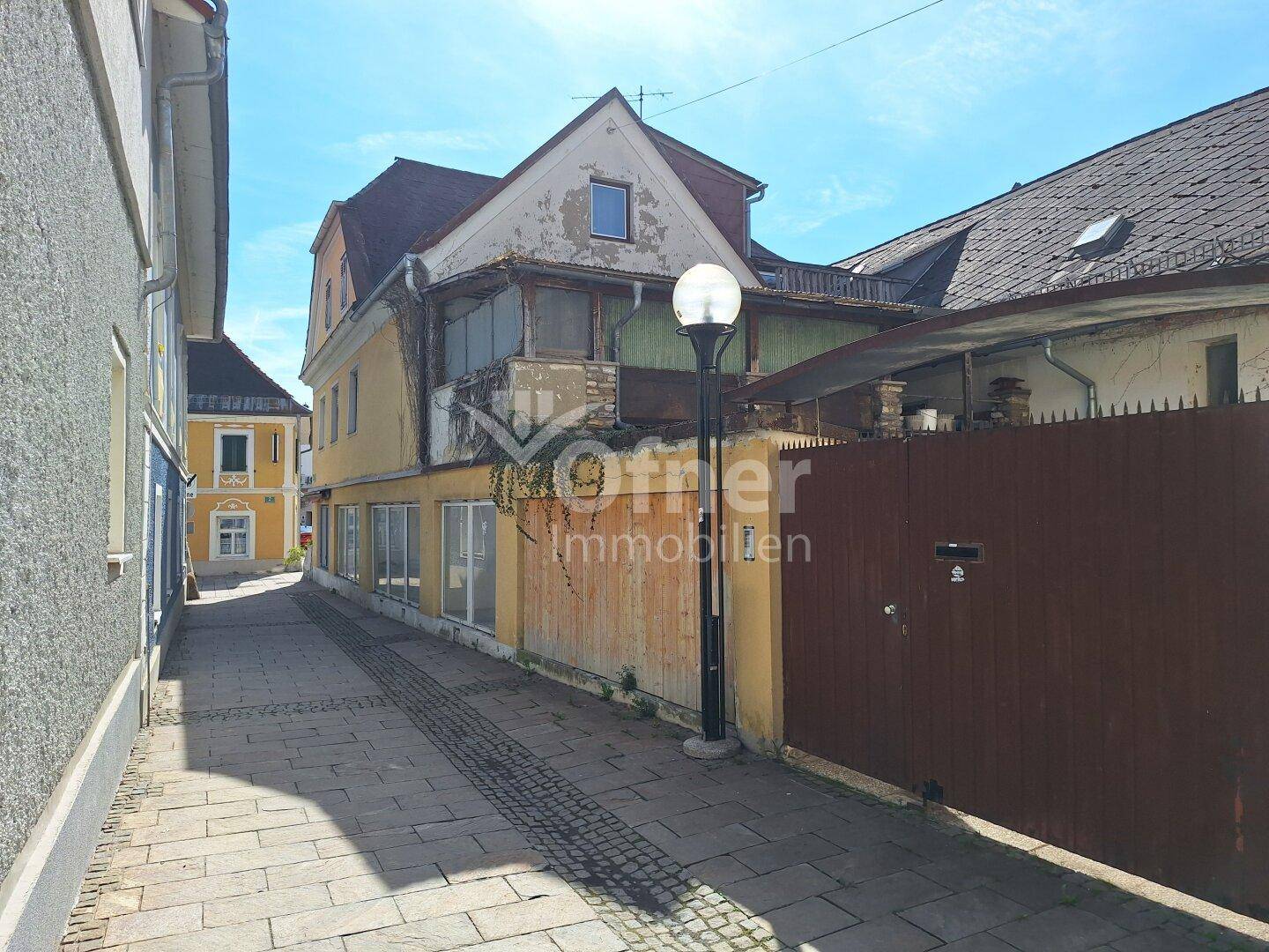 Schmale Gasse zwischen Gebäuden mit gelber und grauer Fassade unter blauem Himmel.