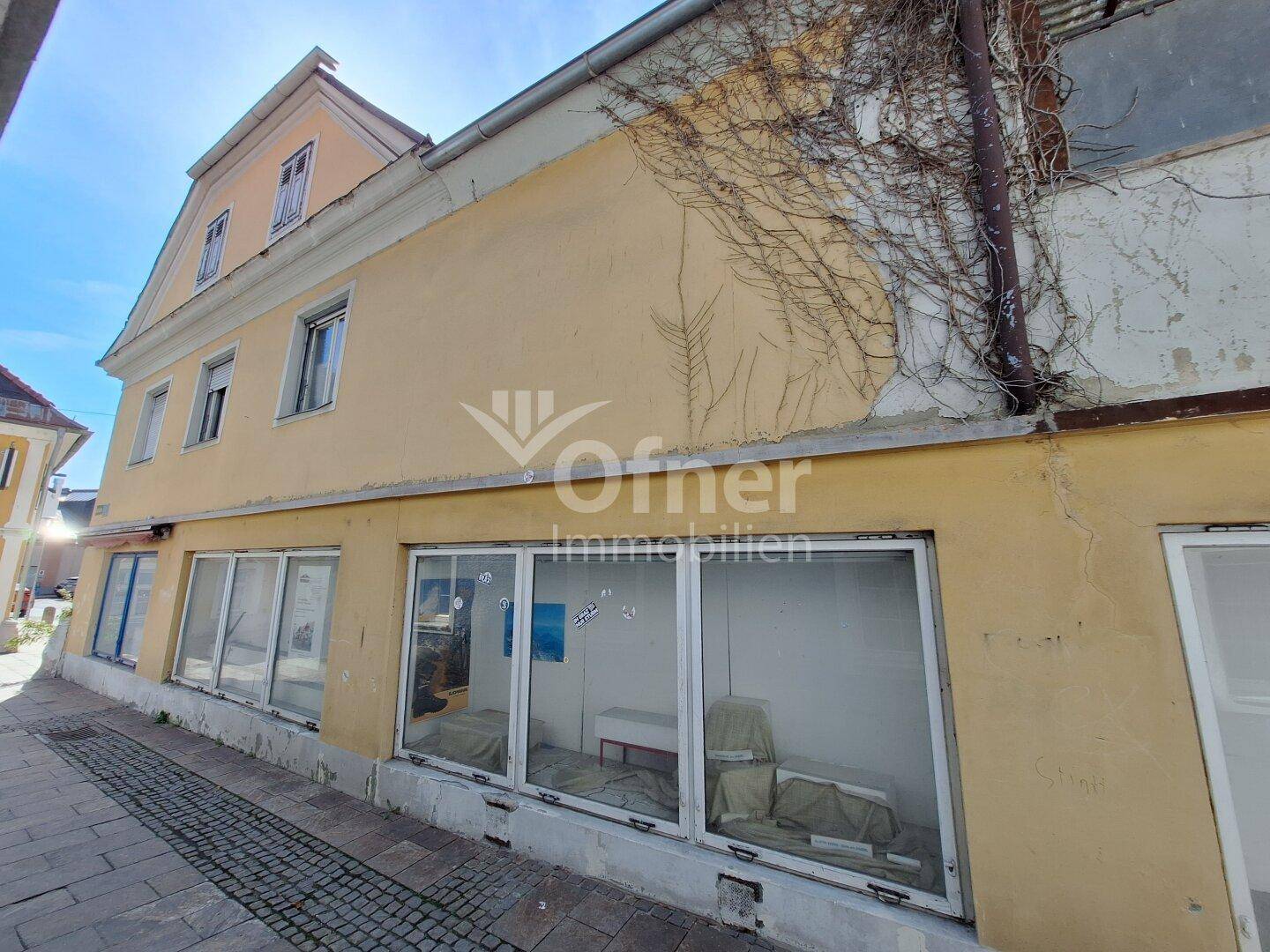 Gelbe Fassade eines älteren Gebäudes mit großen Schaufenstern im Erdgeschoss.