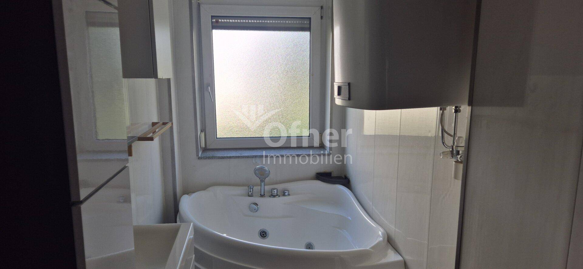 Badezimmer mit Eckbadewanne, Duschfunktion und Fenster für Tageslicht.
