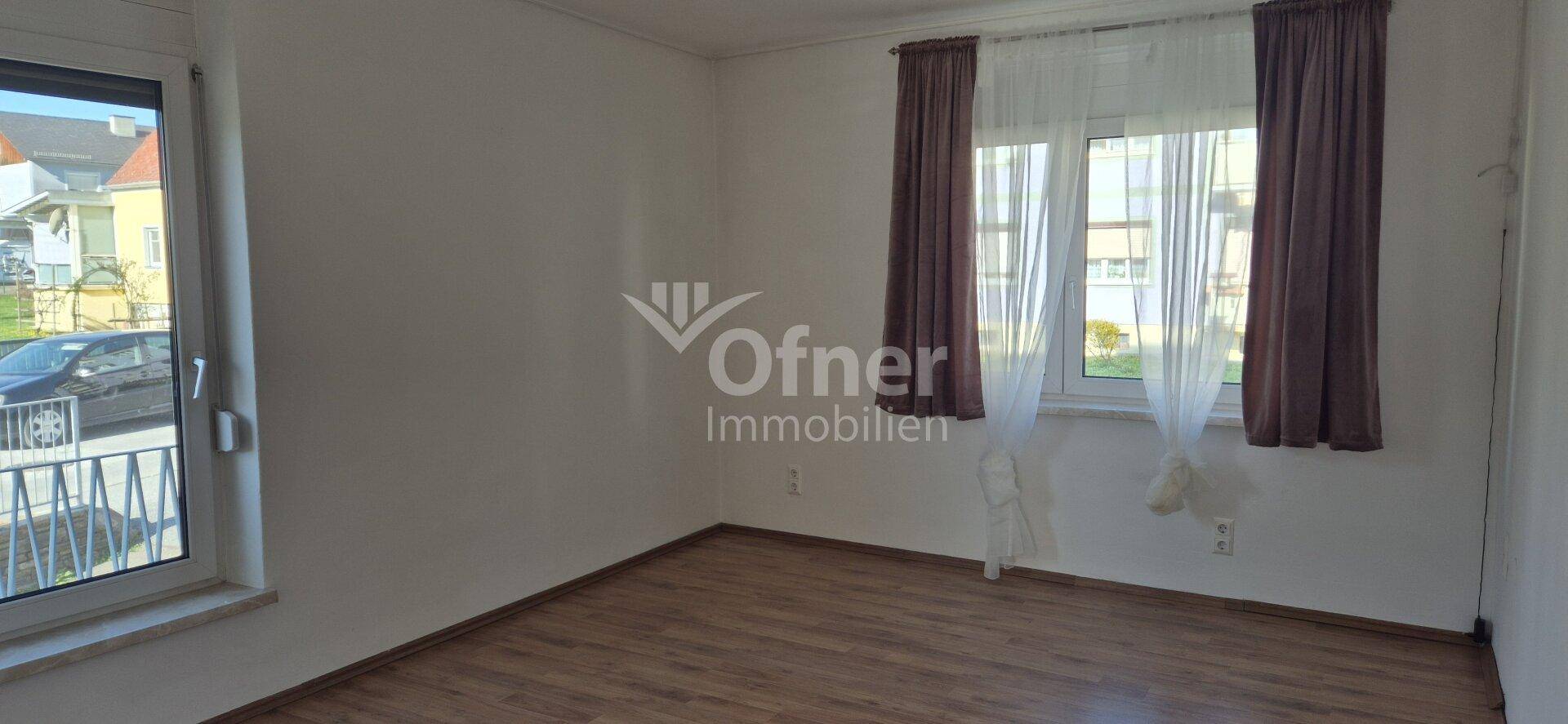 Leeres Zimmer mit Laminatboden, großem Fenster und Blick auf die Straße.