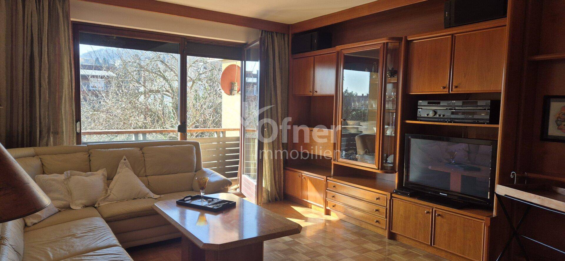 Gemütliches Wohnzimmer mit beigem Sofa, Holzmöbeln und Zugang zu einem sonnigen Balkon.
