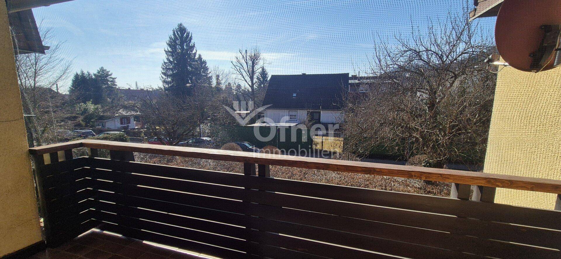 Balkon mit Holzboden und Blick ins Grüne sowie auf die umliegenden Häuser.