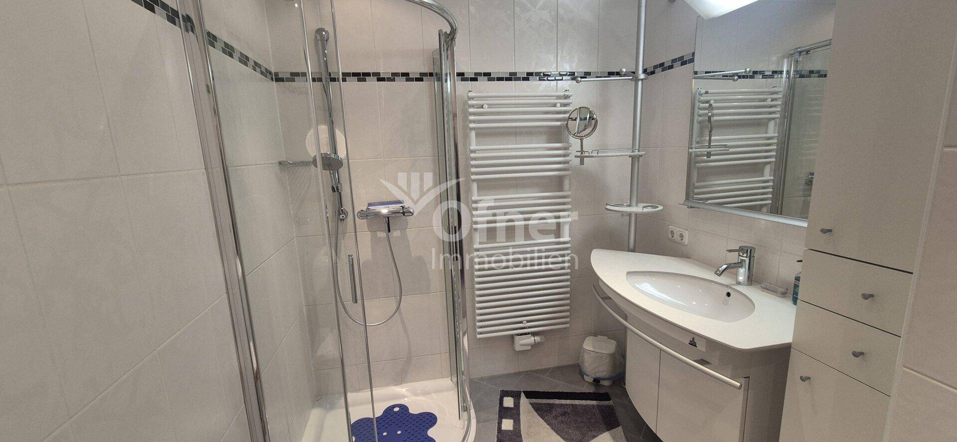 Modernes Badezimmer mit Duschkabine, Waschbecken und beheiztem Handtuchhalter.