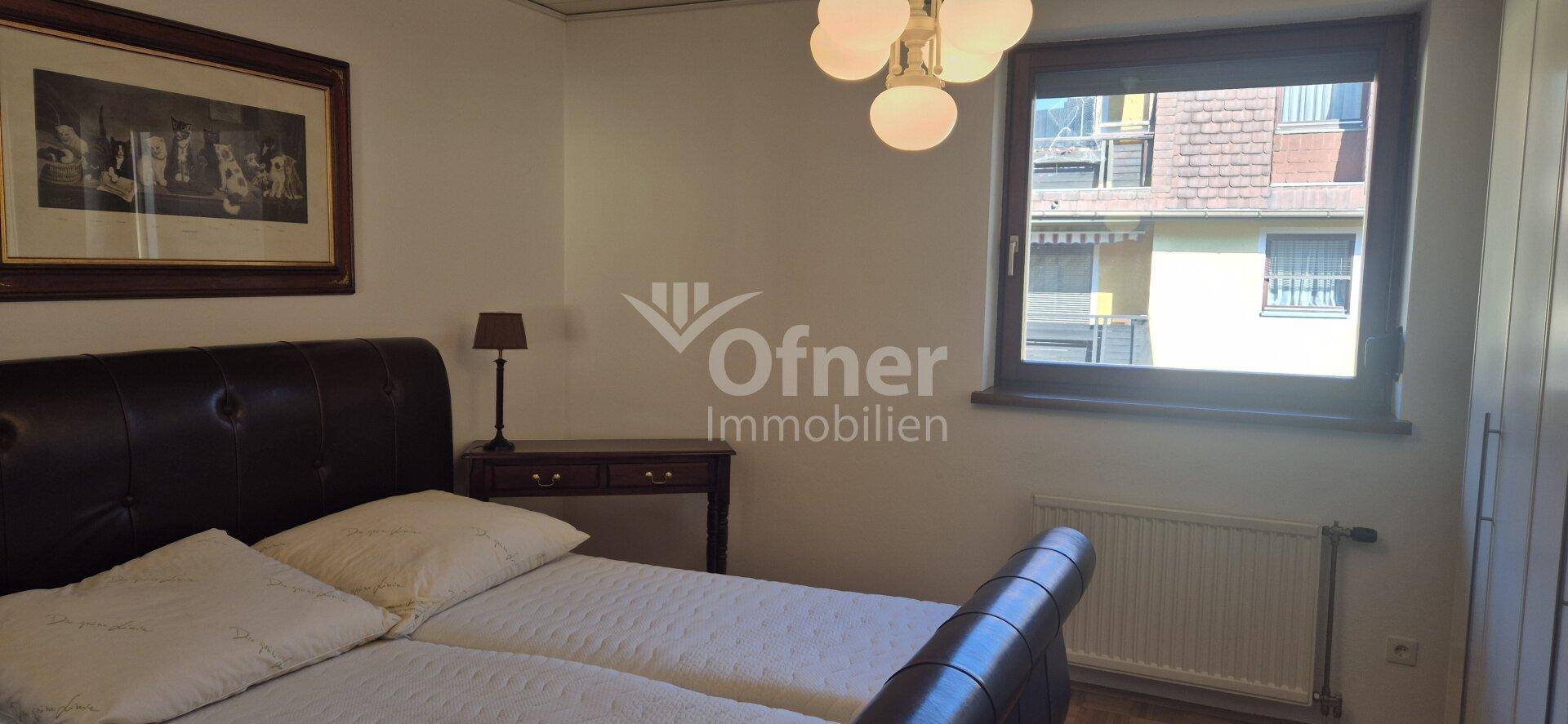 Schlafzimmer mit Doppelbett, Nachttisch und Fenster, das viel Tageslicht hereinlässt.