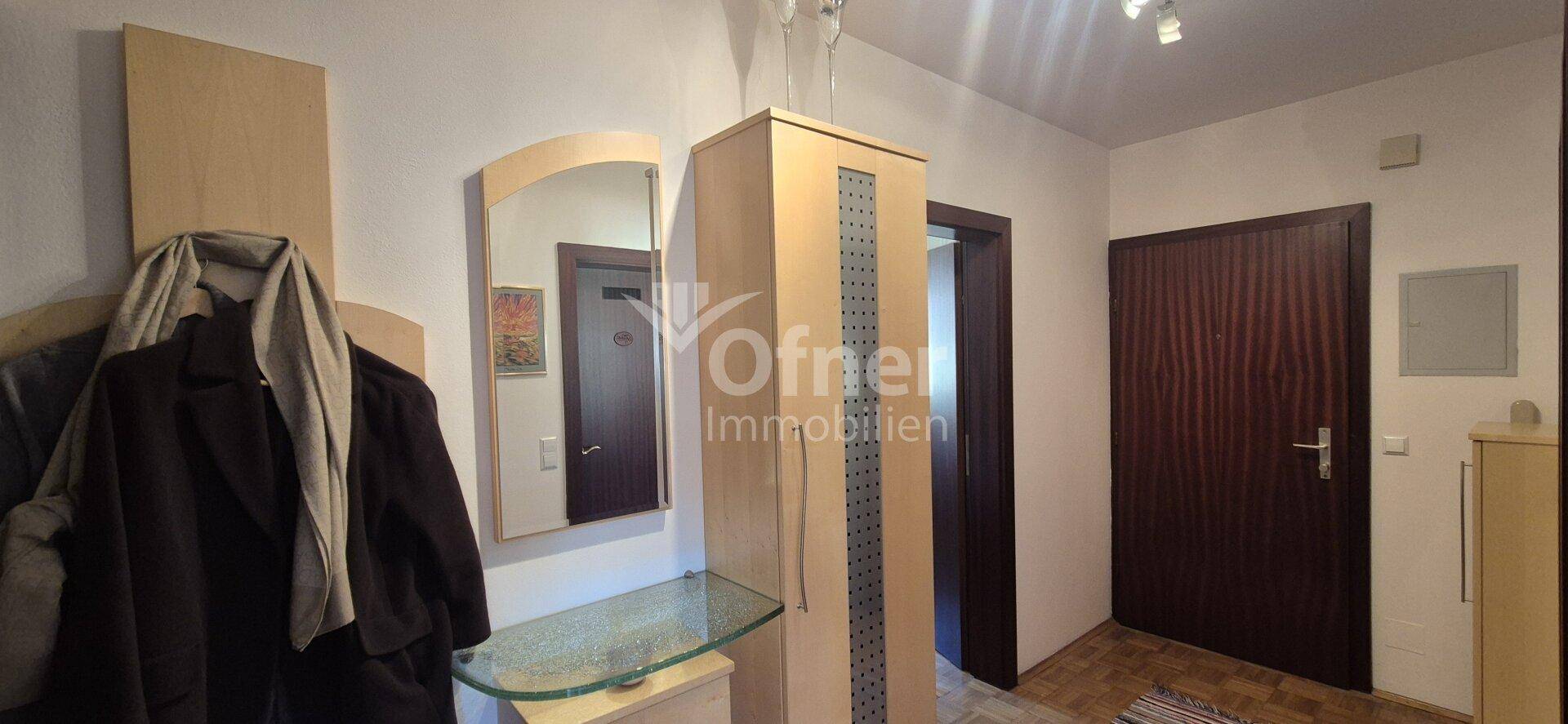 Heller Flur mit Spiegel, Garderobe und Holztüren, die zu weiteren Räumen führen.