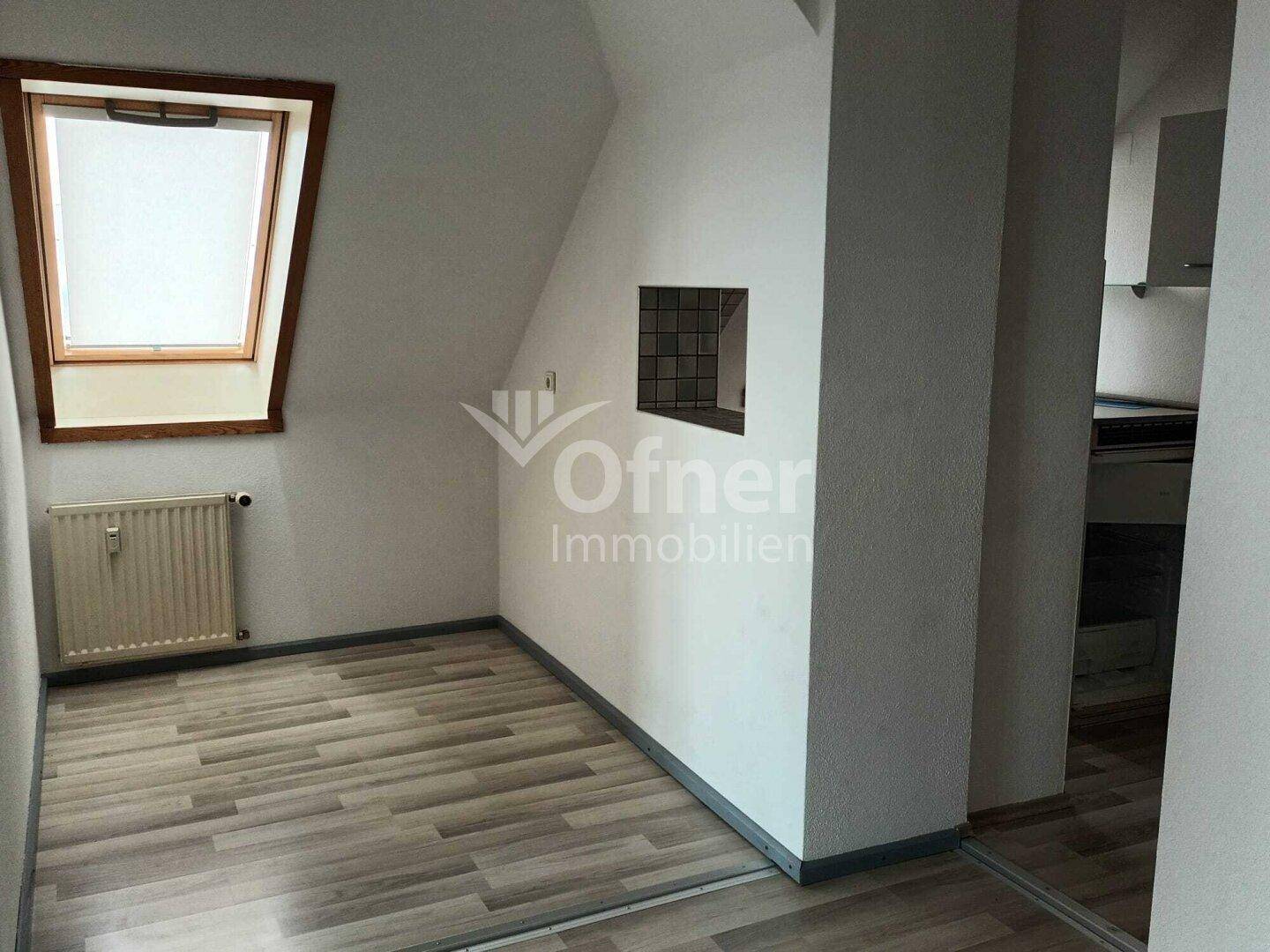 Leeres Zimmer mit Dachfenster, Heizkörper und hellem Laminatboden, ideal als Schlafzimmer.