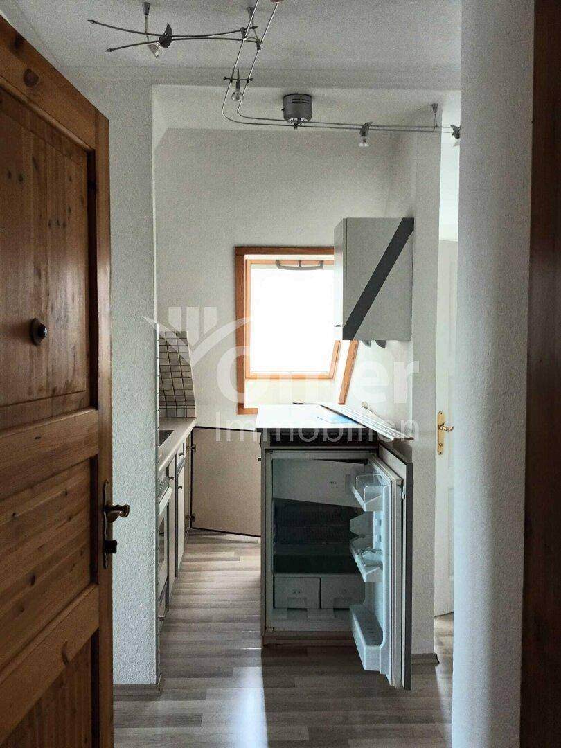 Kleine Küchenzeile mit Kühlschrank, Spüle und Dachfenster, praktisch und funktional.