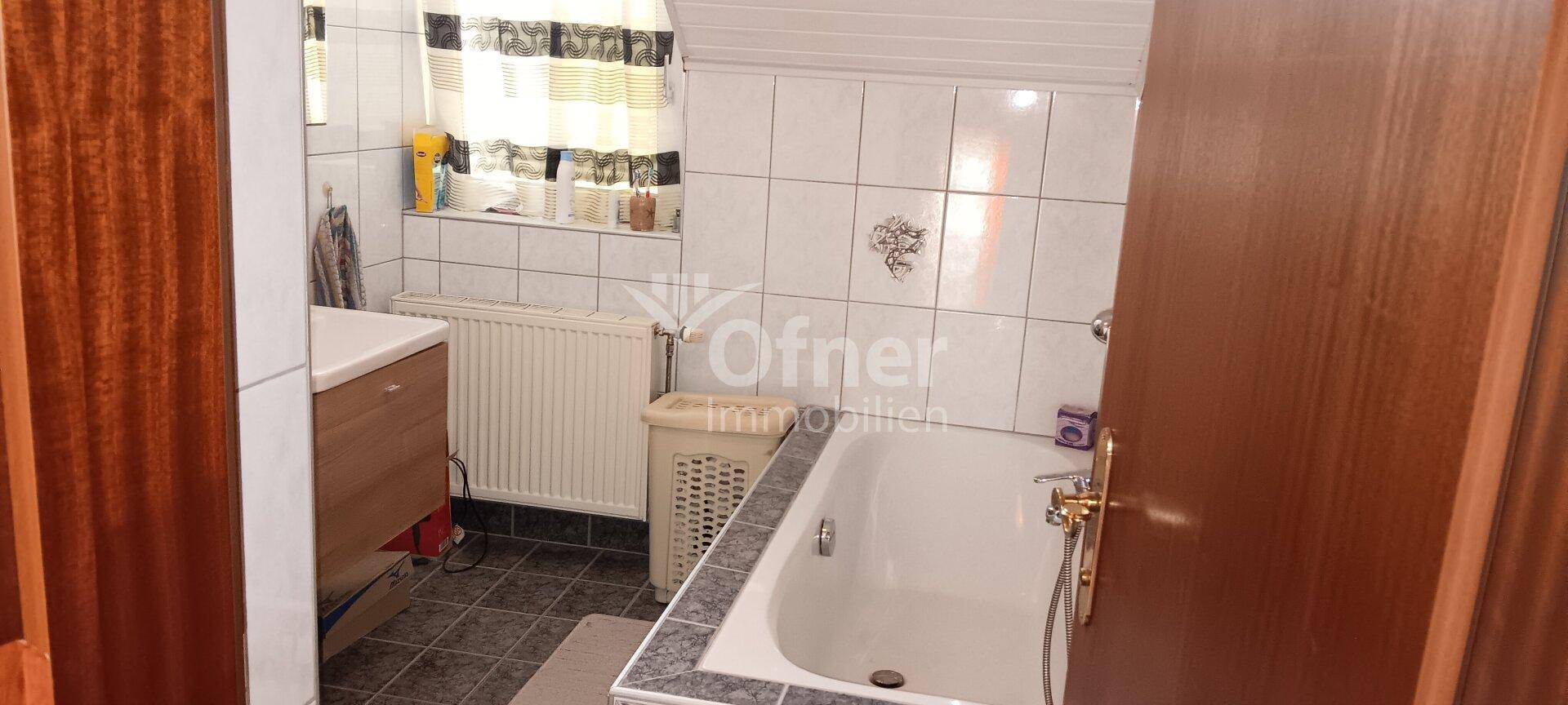 Badezimmer mit Badewanne, Waschbecken und Fenster, gefliest in hellem Muster.