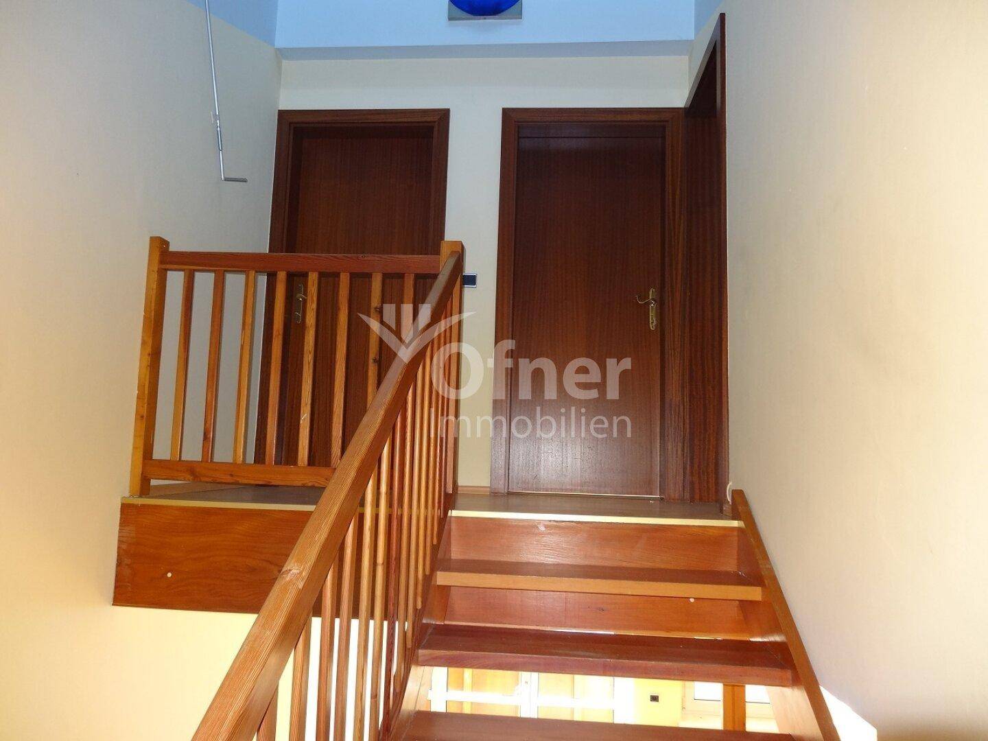 Holztreppe mit Geländer führt zu weiteren Räumen im Obergeschoss.