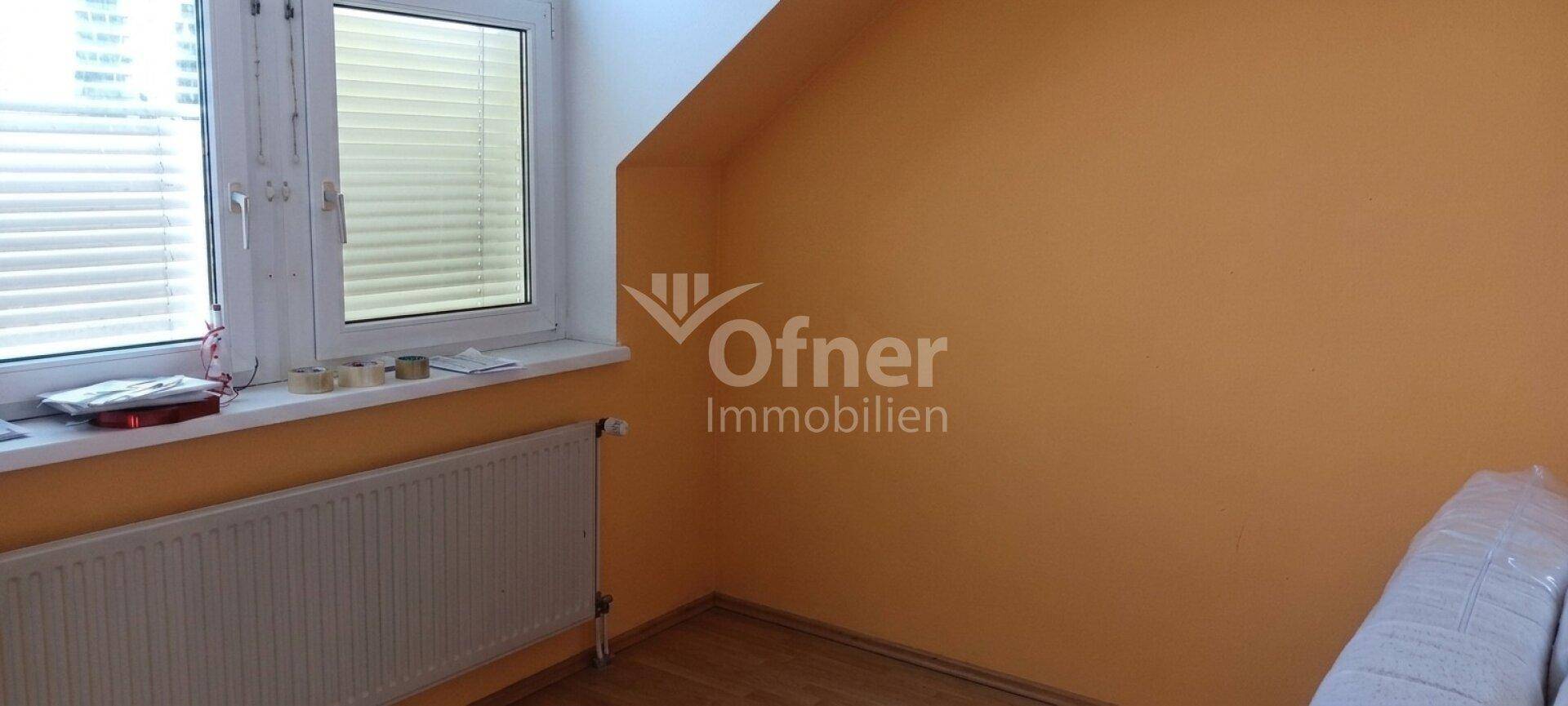Heller Raum mit orangefarbenen Wänden, großem Fenster, Heizkörper und charakteristischer Dachschräge, ideal für ein Schlafzimmer.