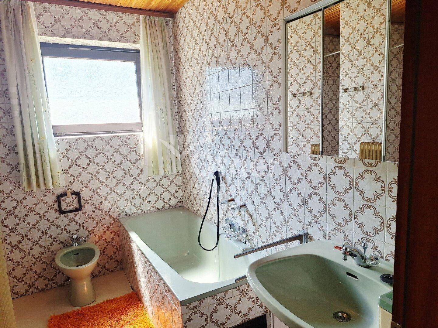 Badezimmer im Stil der 80er Jahre mit Badewanne, Bidet und gemusterten Fliesen.