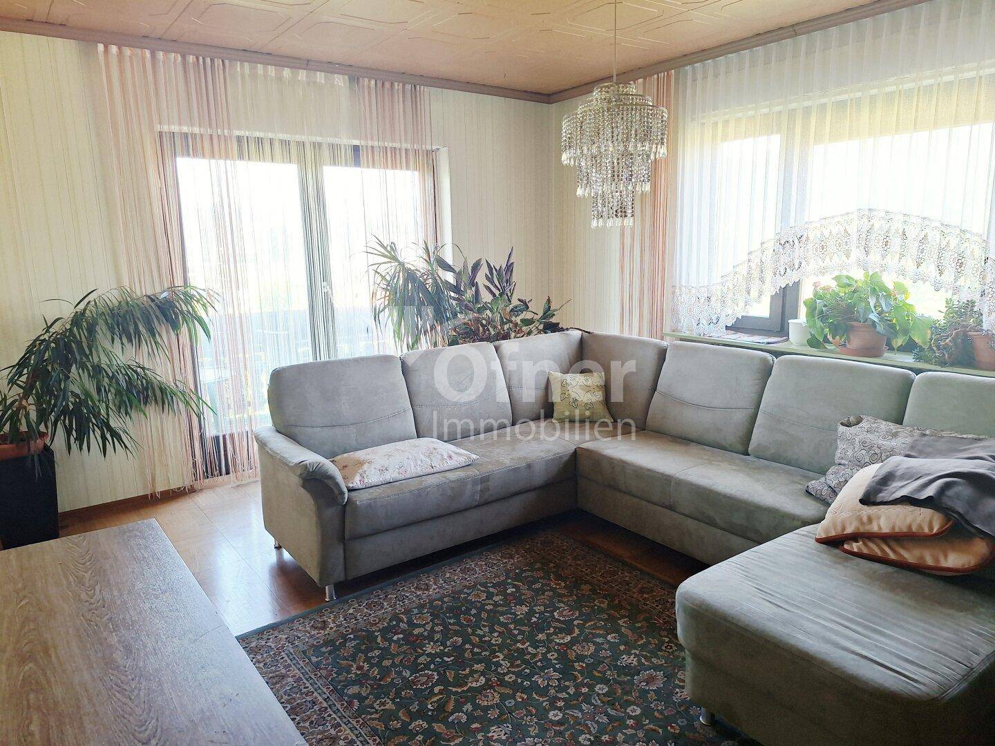 Helles Wohnzimmer mit großem Ecksofa, Kronleuchter und Zugang zum Balkon.