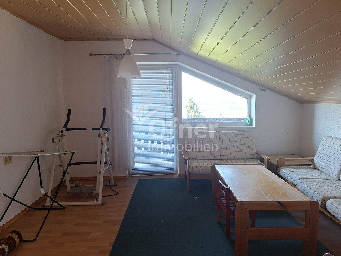 Heller Wohnbereich im Dachgeschoss mit Holzdecke, Dachschräge und großem Fenster.