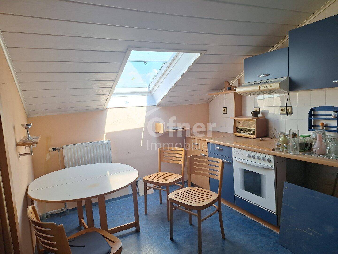 Kleine Küche im Dachgeschoss mit Essbereich, Dachfenster und blauen Schränken.