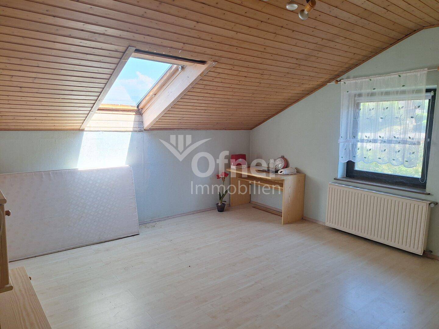 Geräumiges Zimmer im Dachgeschoss mit Holzdecke, Dachschräge und viel Tageslicht.