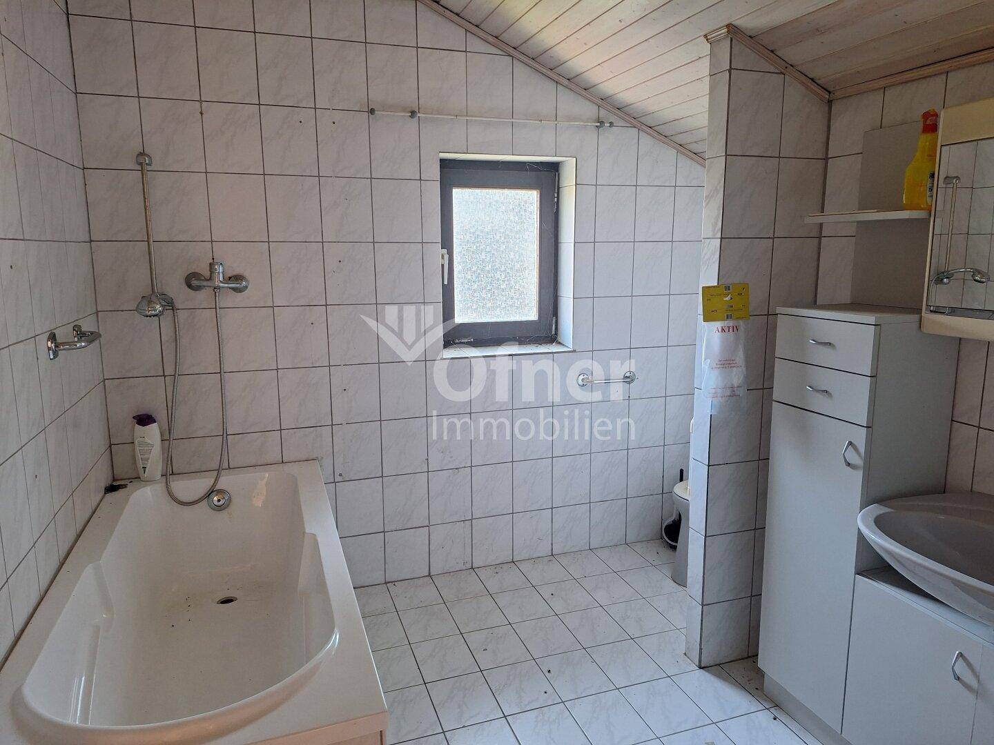 Badezimmer im Dachgeschoss mit Badewanne, Fliesen und Dachschräge.