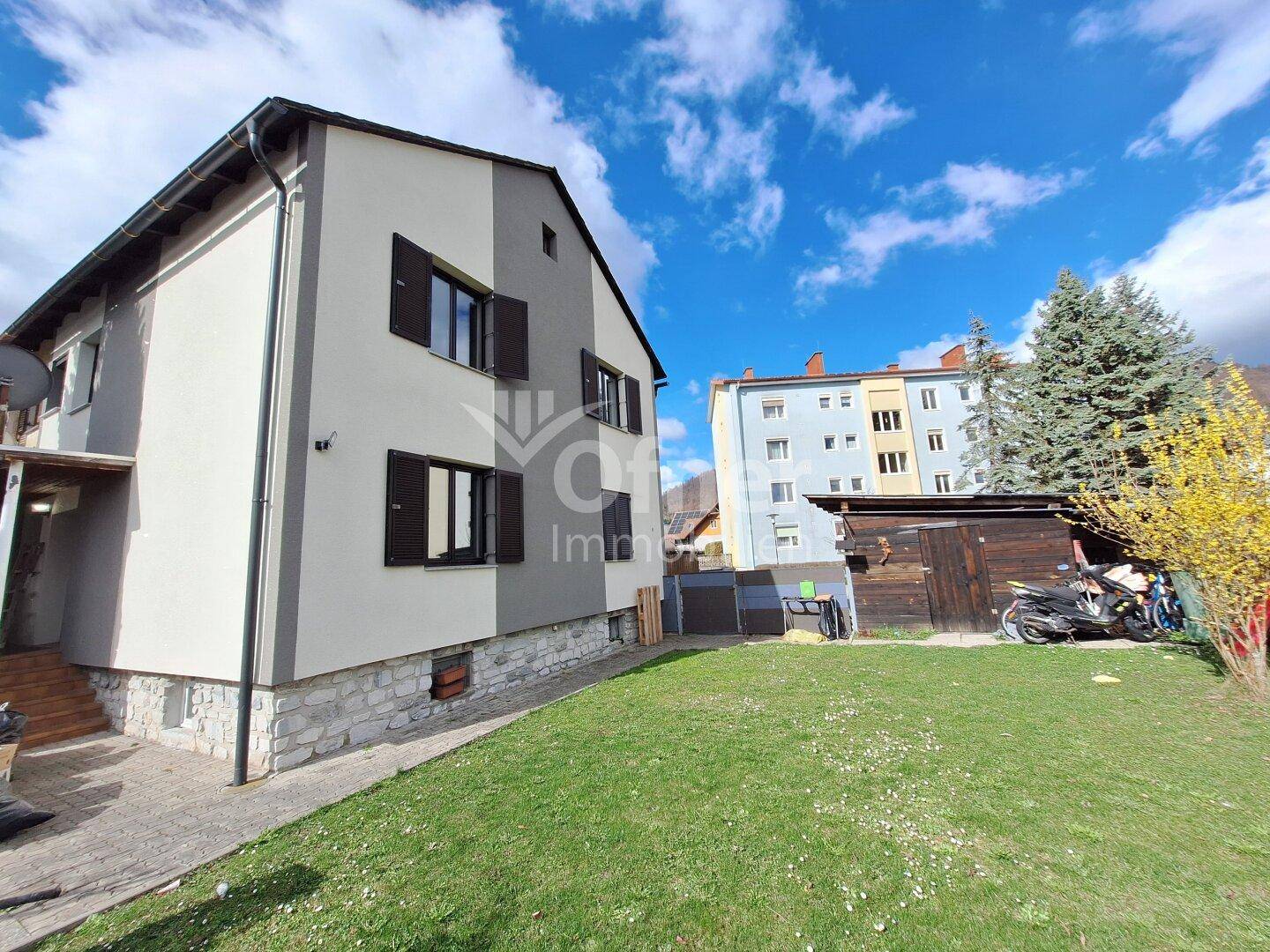 Seitenansicht des Hauses mit großem Rasenbereich und einem Schuppen im Hintergrund.