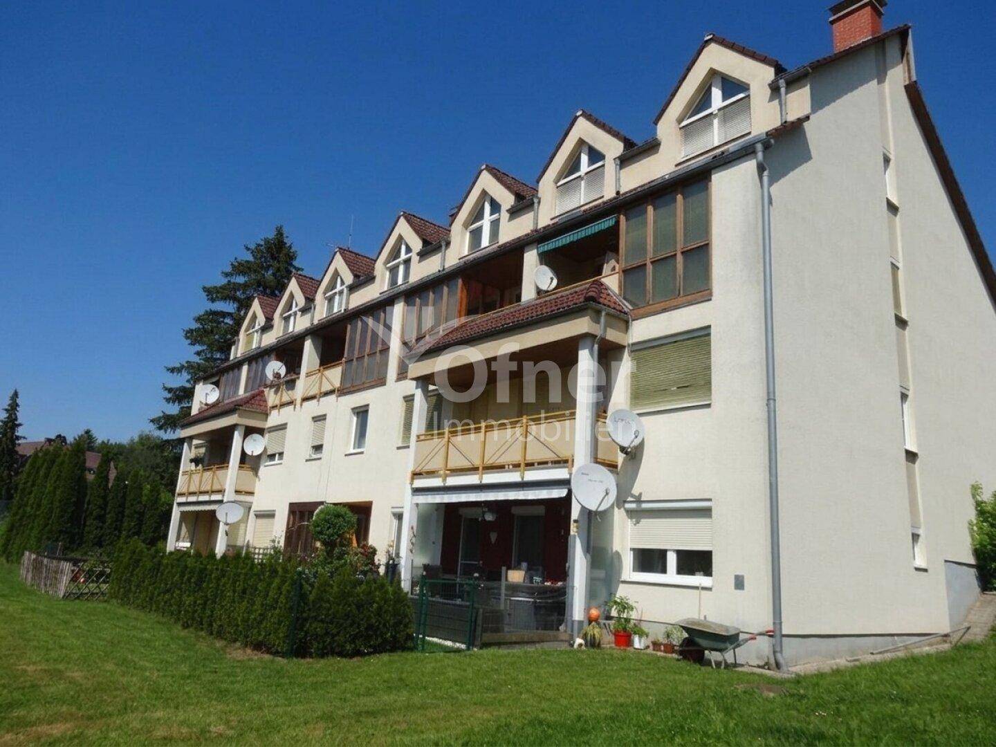 Mehrfamilienhaus mit mehreren Balkonen und Dachgauben, umgeben von einer Grünfläche.