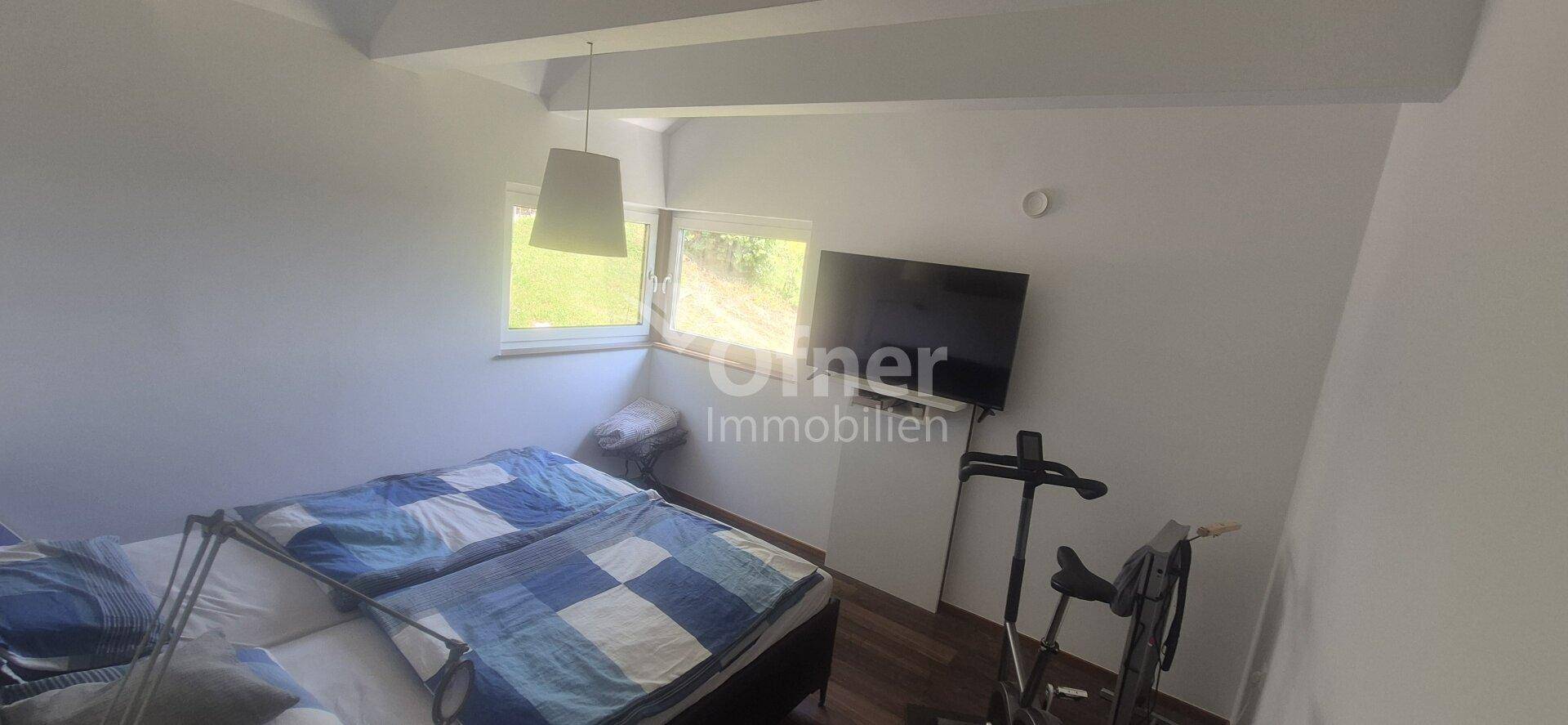 Schlafzimmer mit Bett, Fernseher und Fenster mit Blick auf die Natur.