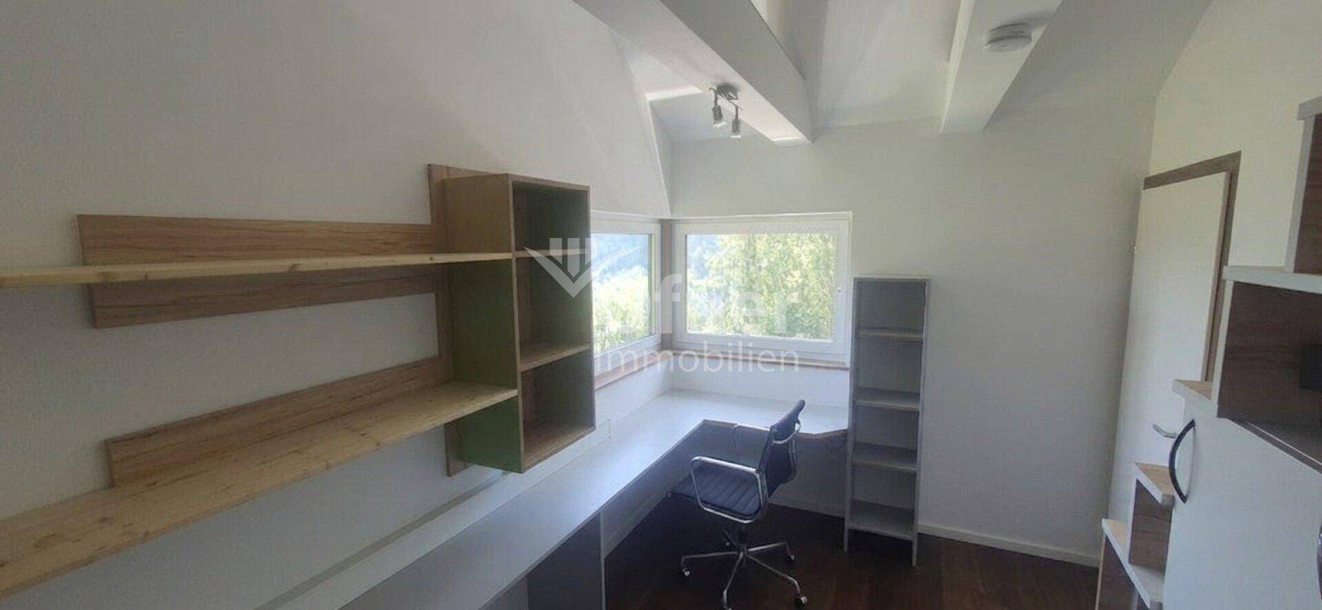 Helles Arbeitszimmer mit Schreibtisch, Regalen und Blick ins Grüne.
