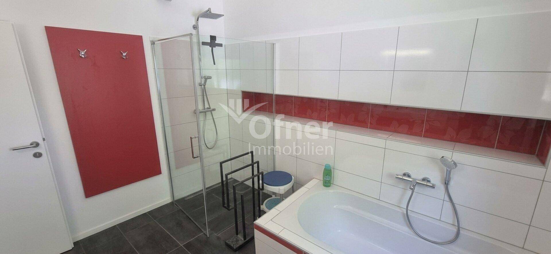 Modernes Badezimmer mit Dusche, Badewanne und roten Akzentfliesen.