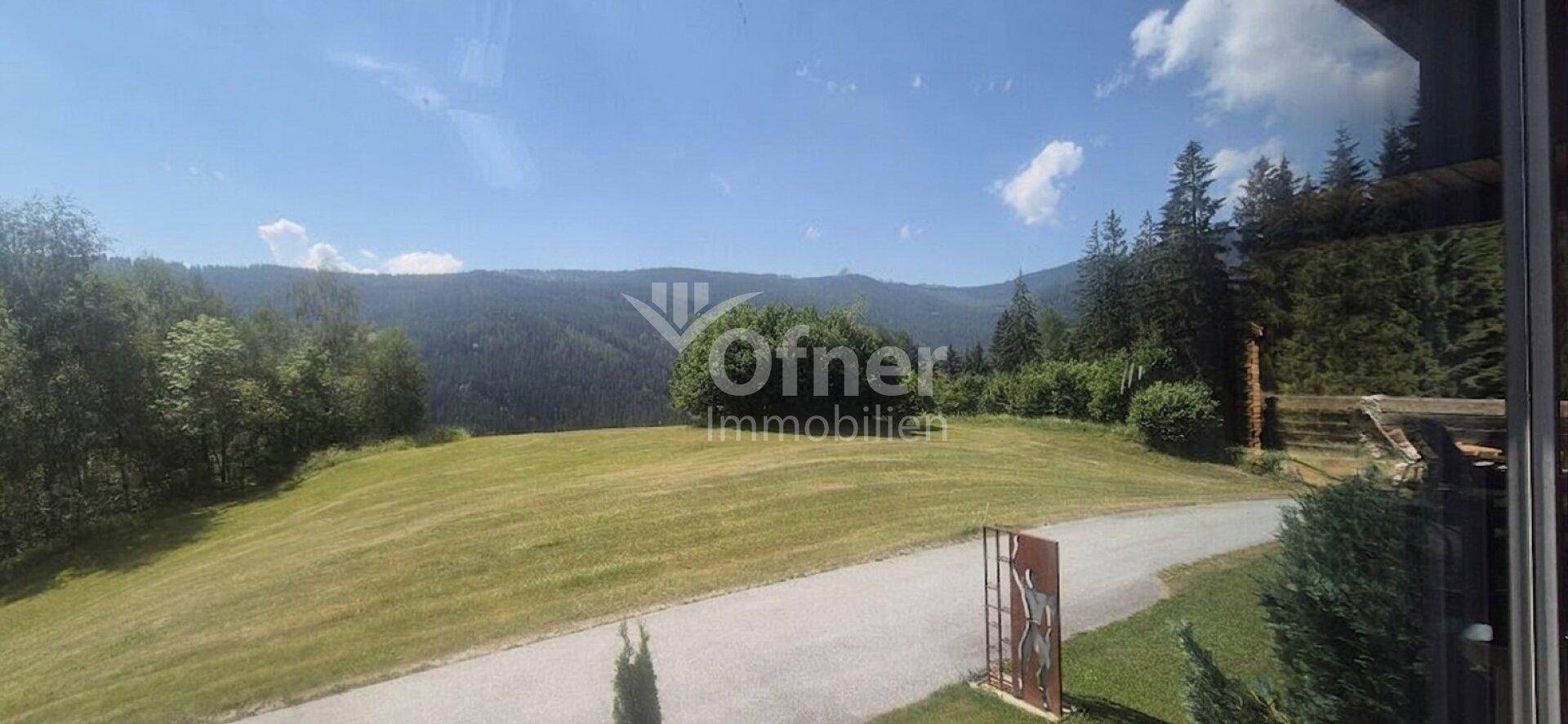 Weitläufiger Blick über grüne Hügel und Wälder unter blauem Himmel.