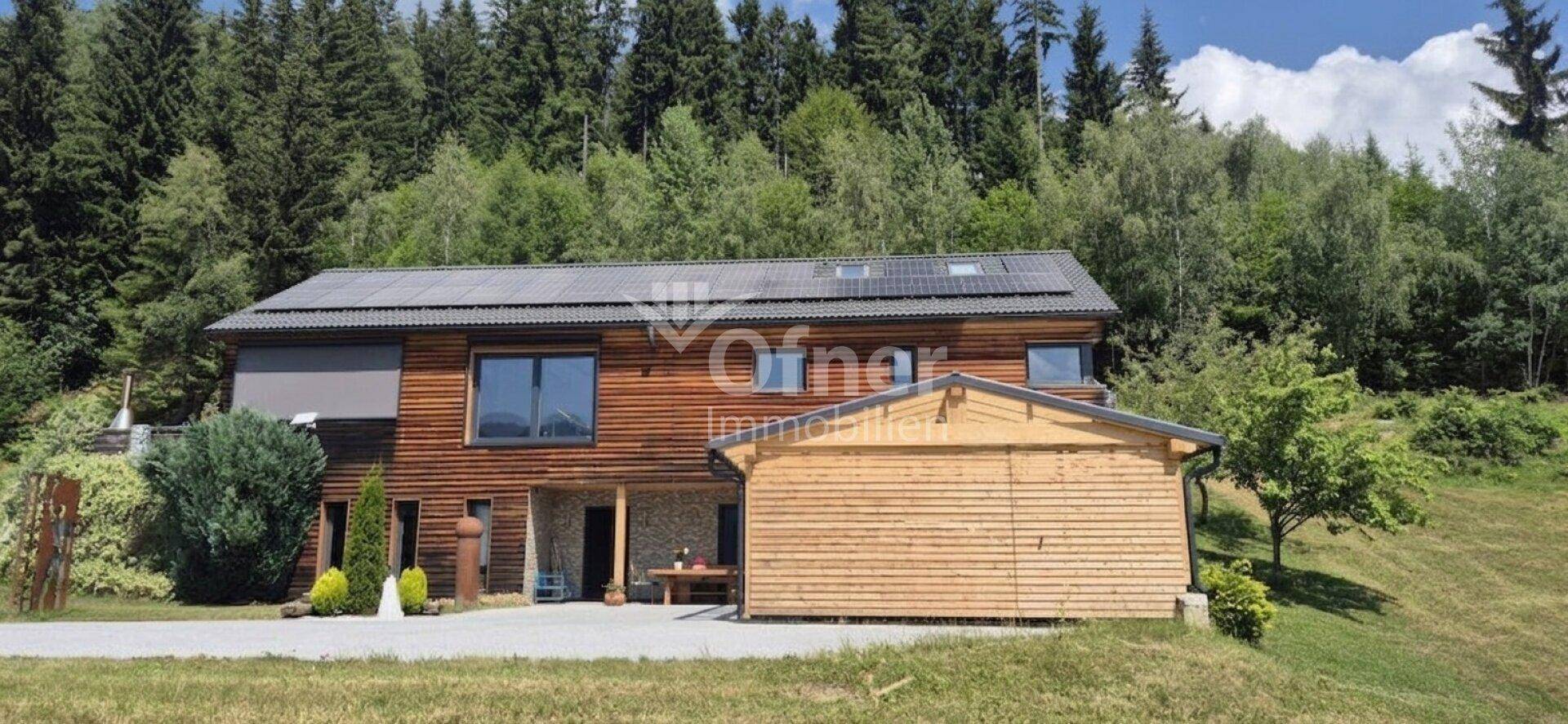 Modernes Holzhaus mit Solaranlage auf dem Dach und angrenzendem Carport.