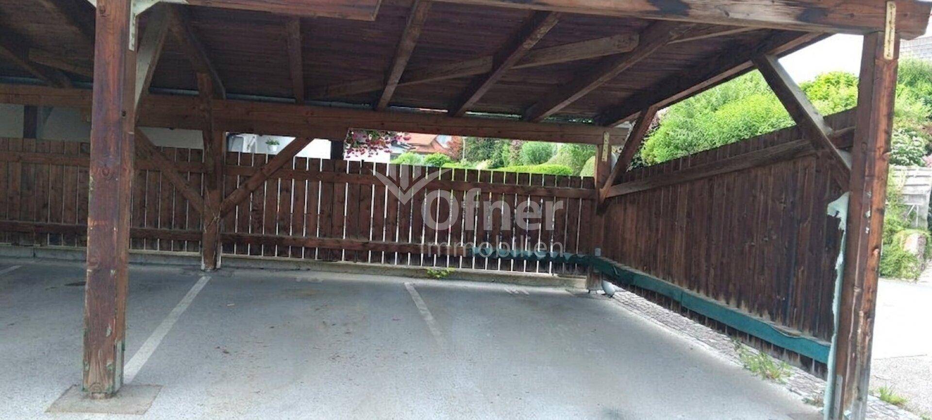 Geräumiger Holzcarport mit mehreren Stellplätzen und Holzzaun im Hintergrund, umgeben von Grün.