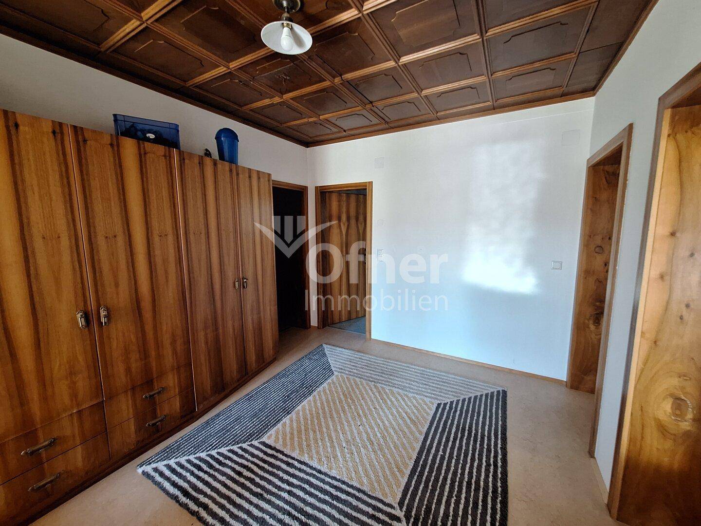 Raum mit großem Holzschrank, Teppich und Holzkassettendecke.