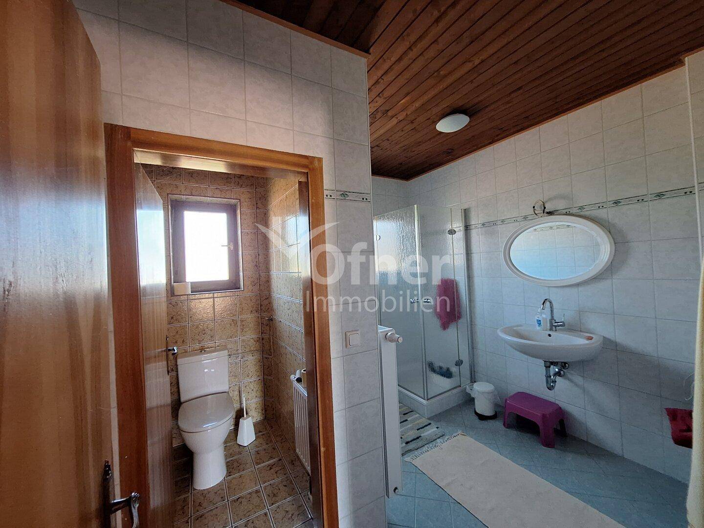 Gefliestes Badezimmer mit Dusche, WC, Waschbecken und Holzdecke.