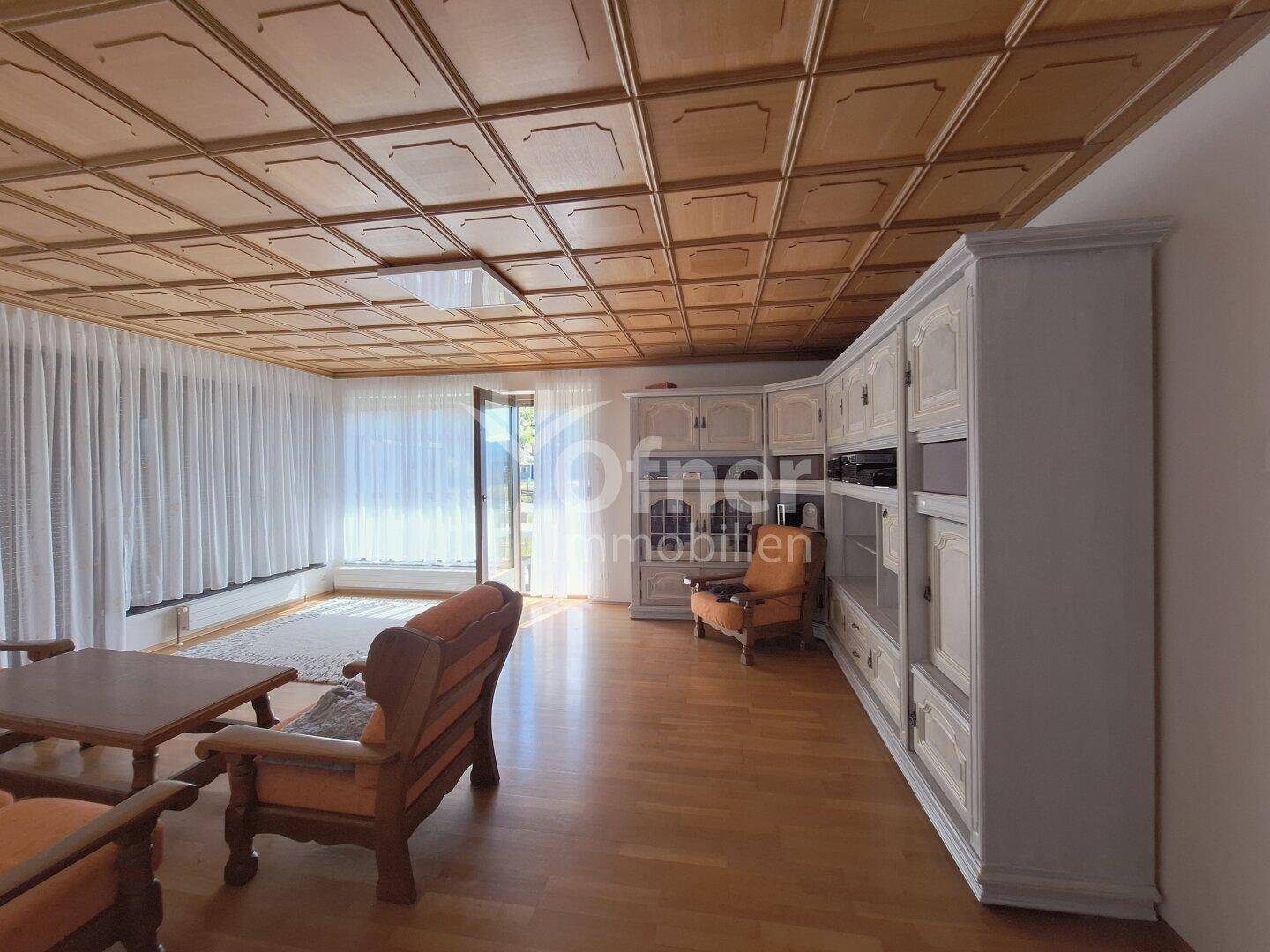 Geräumiges Wohnzimmer mit Holzkassettendecke, Parkettboden und großem Einbauschrank.