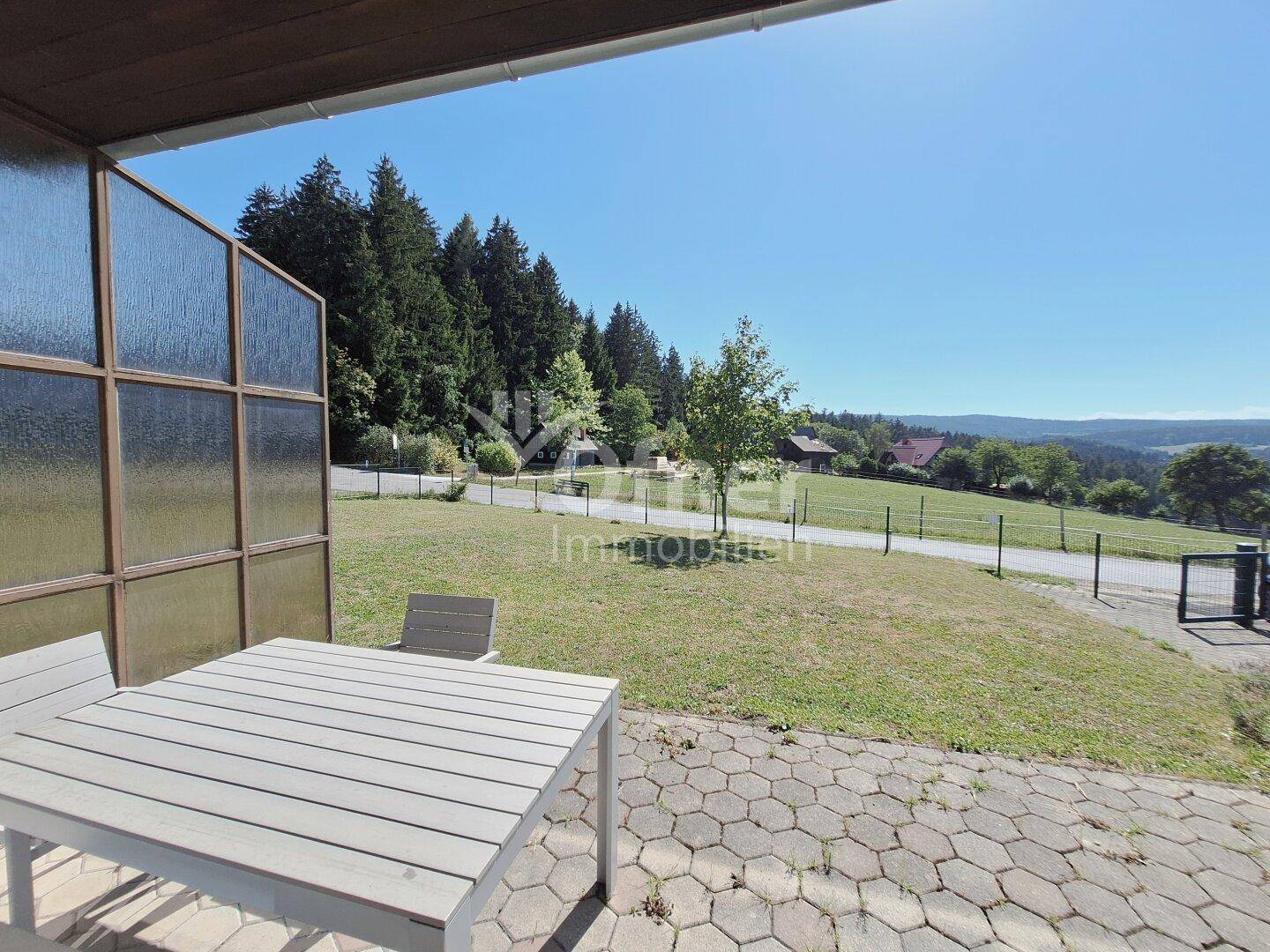 Terrasse mit Esstisch und weitem Blick über die grüne Hügellandschaft.