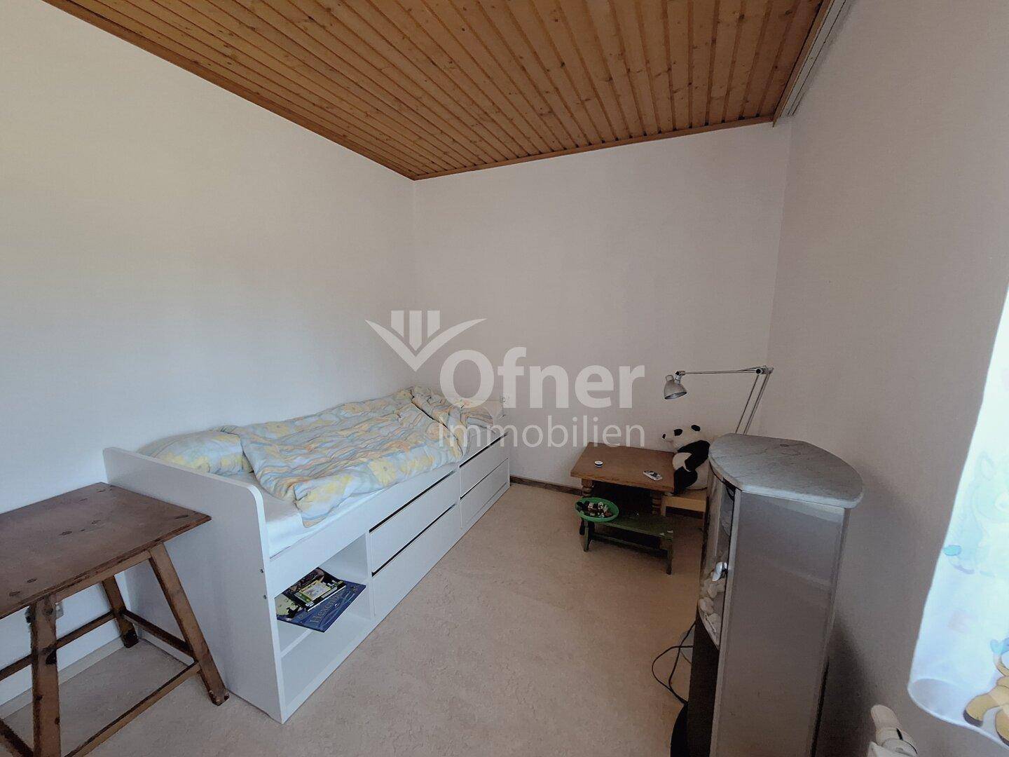 Helles Kinderzimmer mit Einzelbett, Holzdecke und schlichten weißen Wänden.