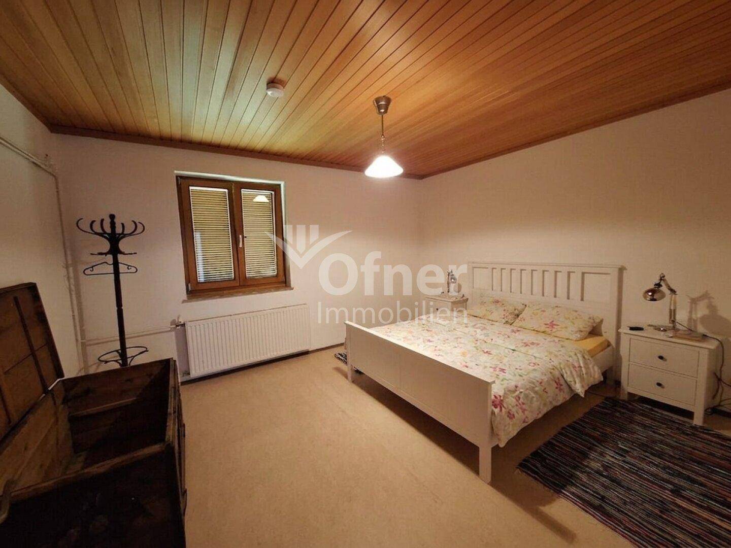 Schlafzimmer mit Holzbalkendecke, Doppelbett und einem Fenster mit Holzrahmen.