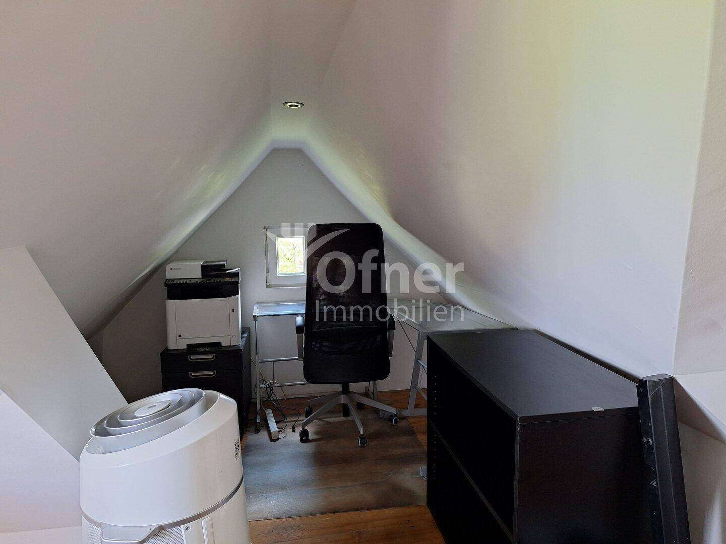 Dachgeschosszimmer als Büro eingerichtet mit Schreibtisch, Drucker und Dachschrägen.