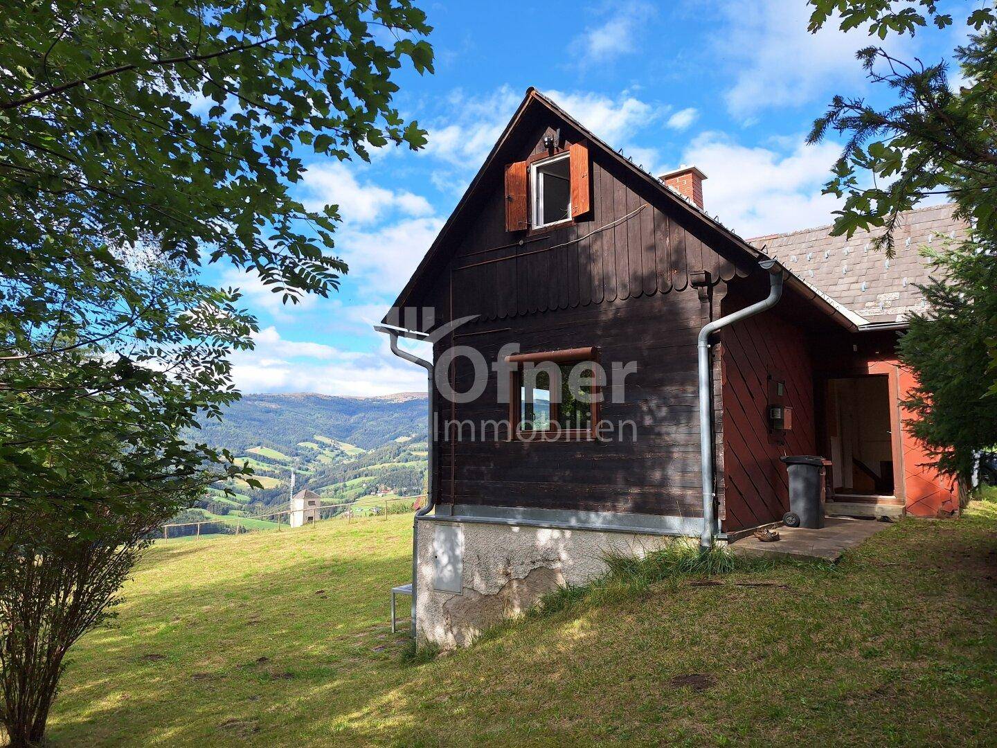 Rustikales Holzhaus mit Satteldach und weitem Blick über die hügelige Landschaft.