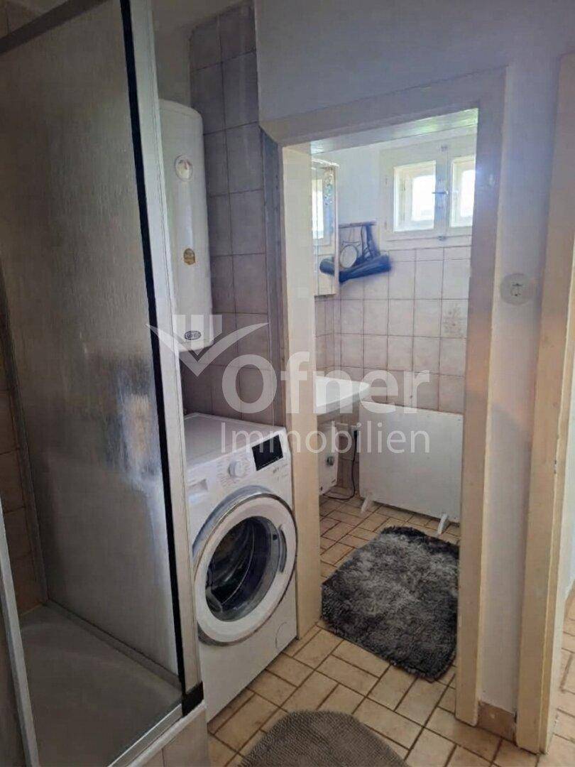 Badezimmer mit Dusche, Waschmaschine und Boiler, gefliest in hellen Farbtönen.