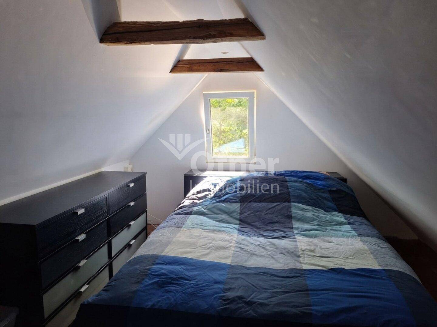 Gemütliches Schlafzimmer im Dachgeschoss mit Bett, Kommode und Dachschrägen.