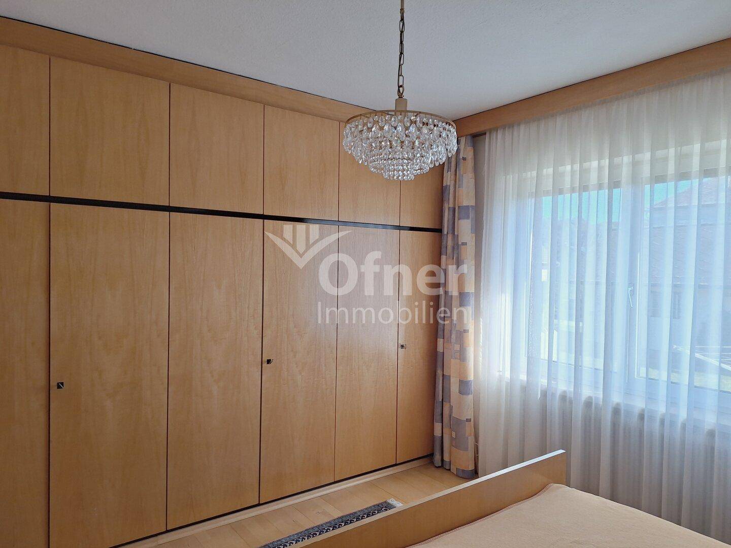 Schlafzimmer mit raumhohen Einbauschränken aus Holz und einem Fenster mit Vorhängen.