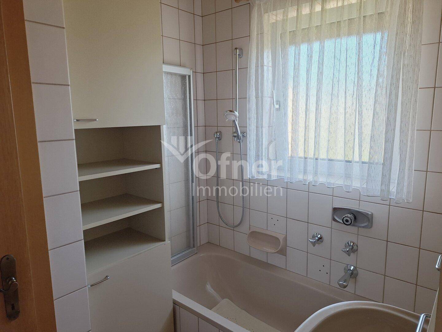 Badezimmer mit Badewanne, Duschvorrichtung, Einzelwaschbecken und hellen Fliesen an den Wänden.
