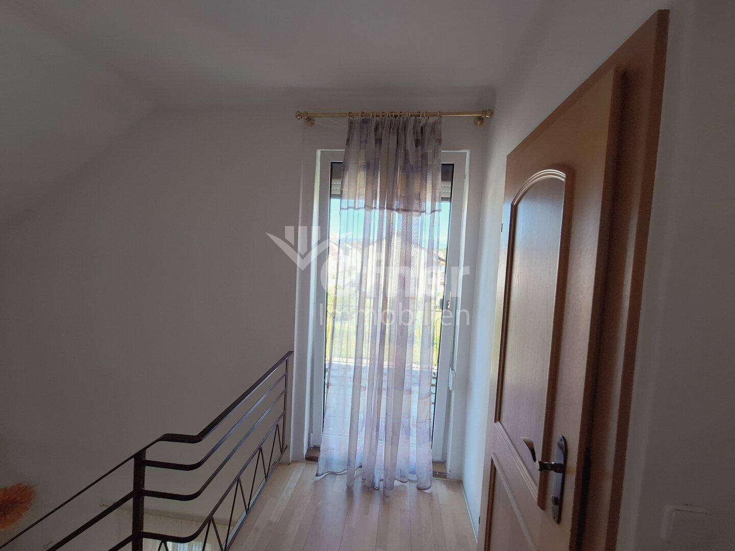 Heller Flur mit Treppenaufgang und einer Tür, die zu einem kleinen Balkon führt.