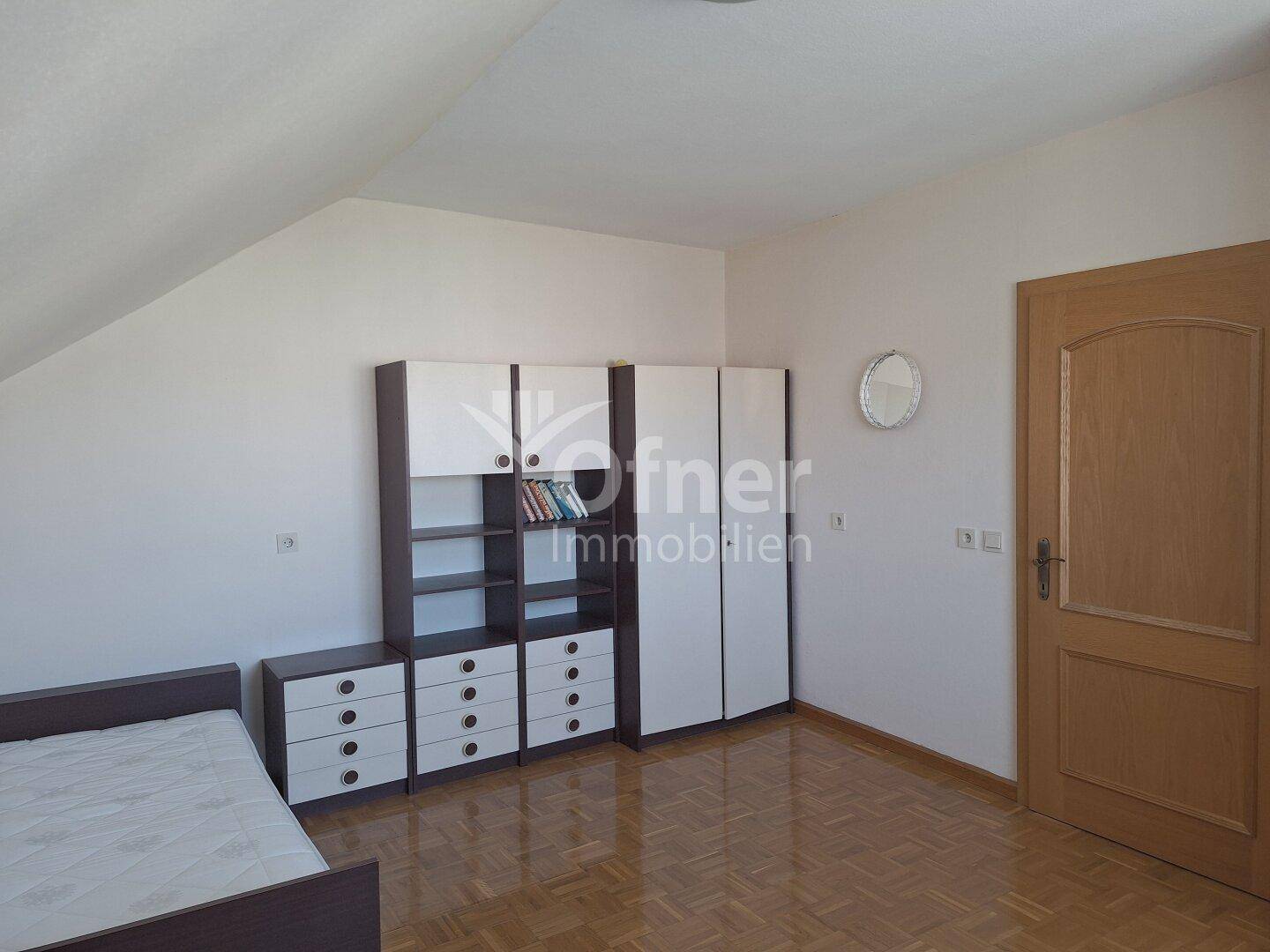 Schlafzimmer mit Einzelbett, modernen Schränken und einer Dachschräge, hell und funktional.