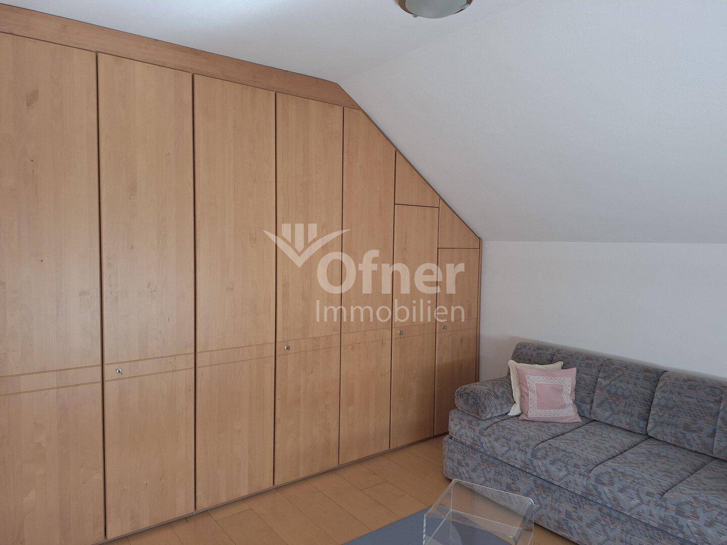 Zimmer im Dachgeschoss mit schrägen Wänden, Einbauschränken aus Holz und einem Sofa.