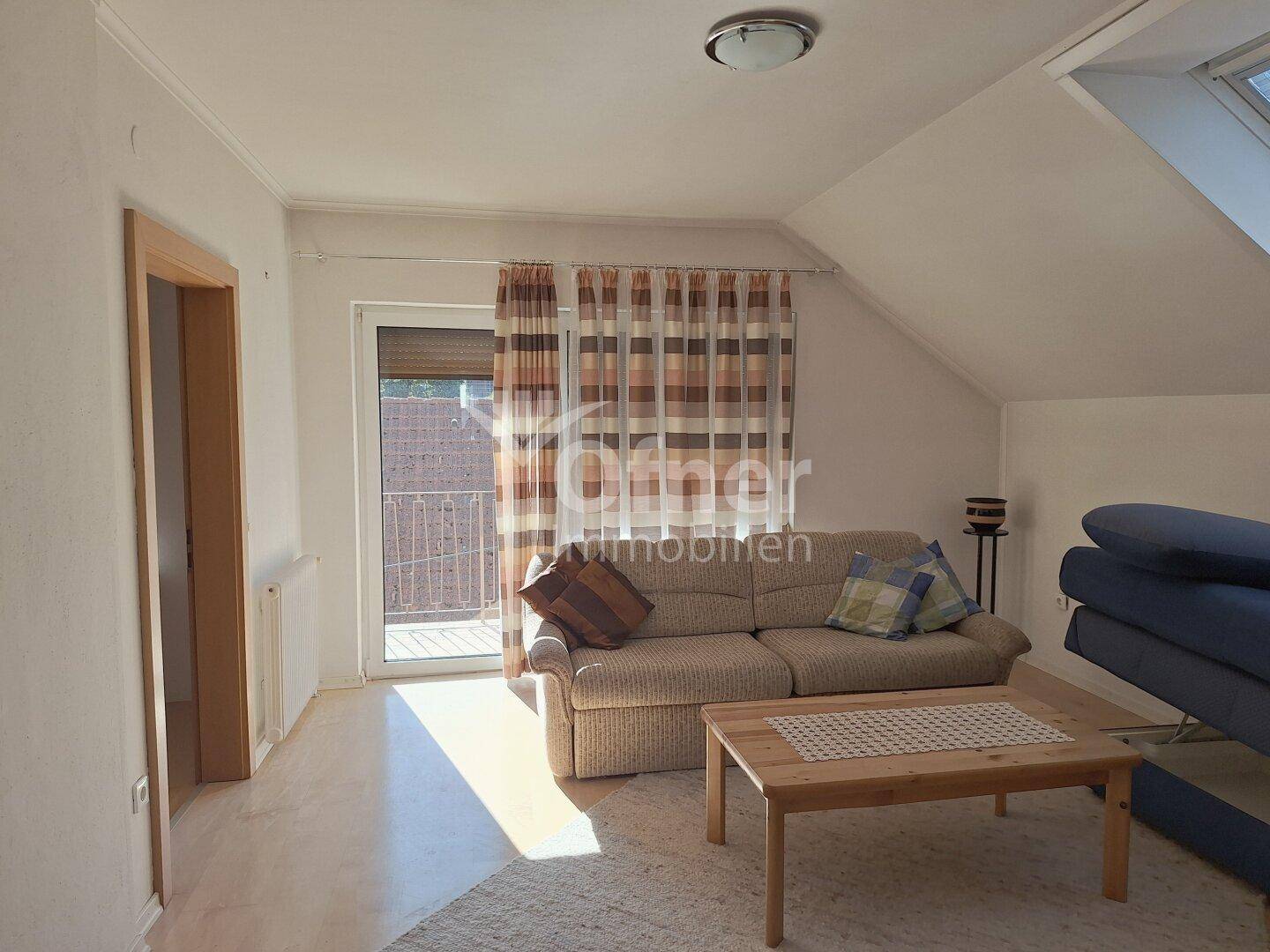 Helles Wohnzimmer im Dachgeschoss mit Sofa, Couchtisch und Zugang zu einem Balkon.