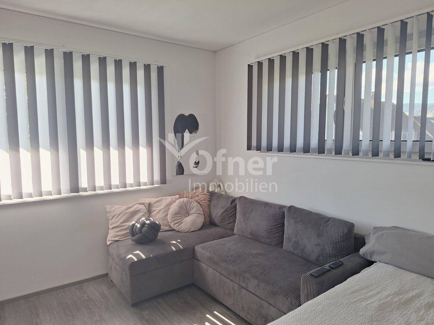 Heller Raum mit Ecksofa, großen Fenstern und modernem Bodenbelag, ideal als Gästezimmer oder Büro.